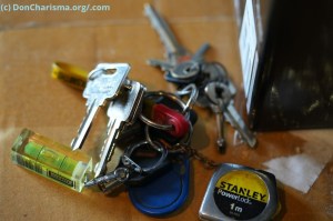 A bunch of keys scattered on a cardboard box, accompanied by a tape measure and a level, creates an intriguing composition that captures the viewer's attention. The keys represent possibility and potential, while the tools suggest measurement and precision, hinting at a sense of organisation and planning. Together, they evoke a feeling of readiness for whatever task may come next.